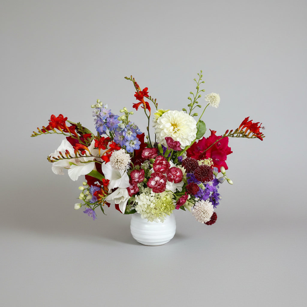Colorful flower arrangement in a white vase on a wooden table with a white wall background